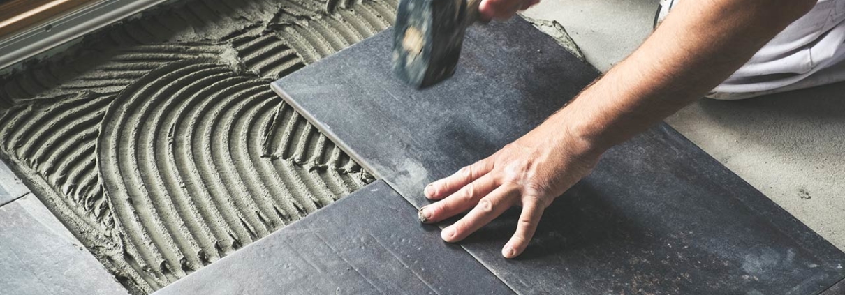 Photo of a worker carefully placing ceramic floor tiles on adhesive surface