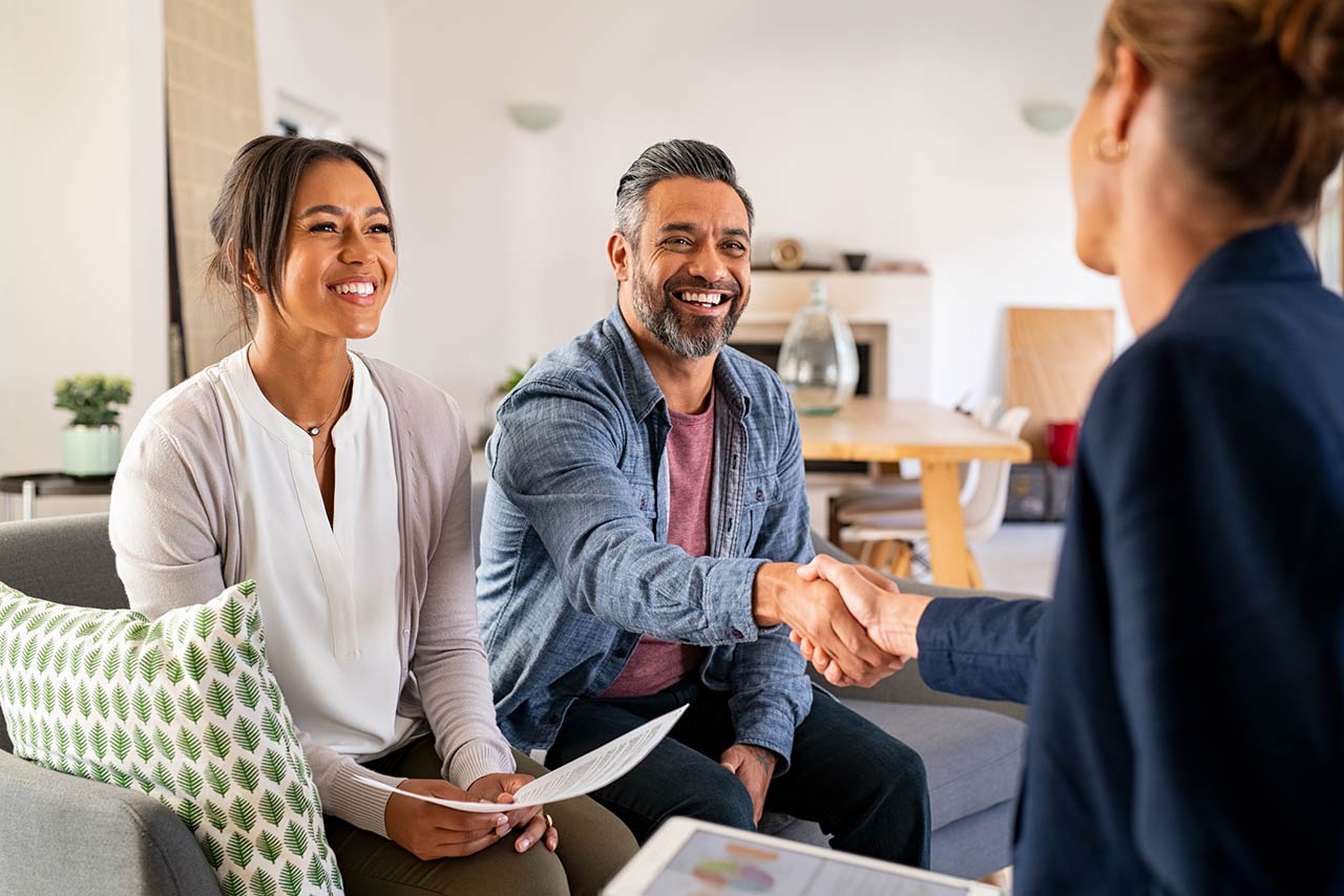 Happy smiling couple greeting broker with handshake at home