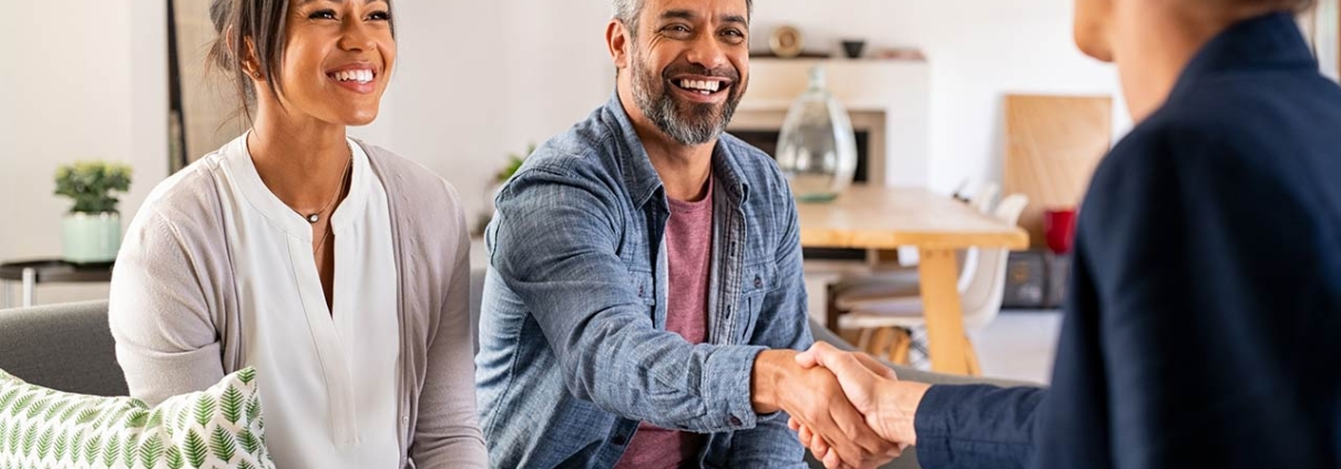 Happy smiling couple greeting broker with handshake at home