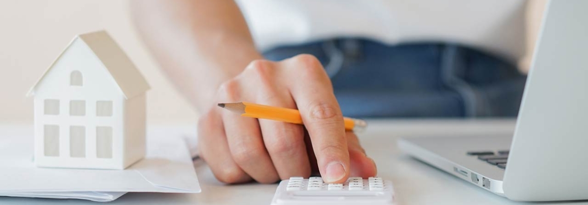 Close up of a mans hand with a pencil calculating with a small home model