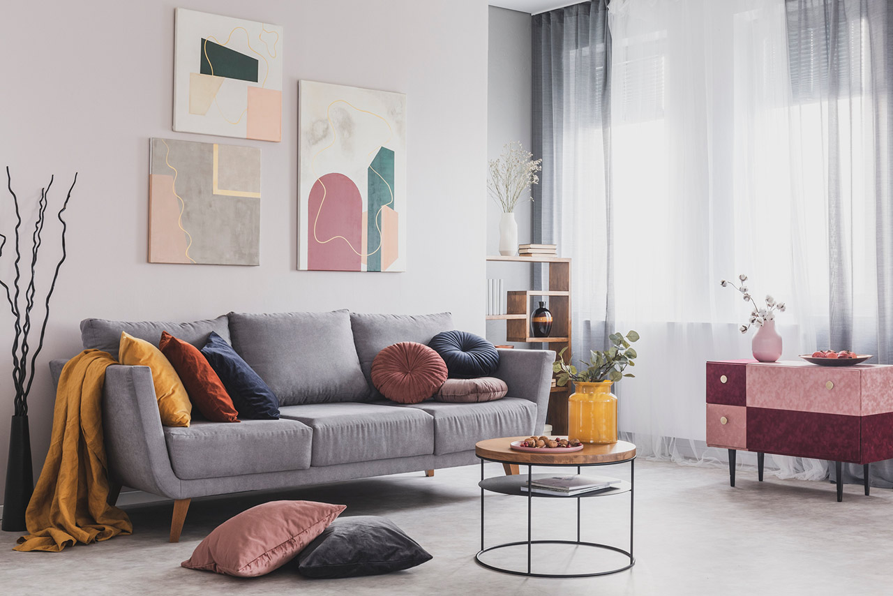 Real photo of abstract paintings hanging on white wall above a gray sofa in a living room interior with big windows