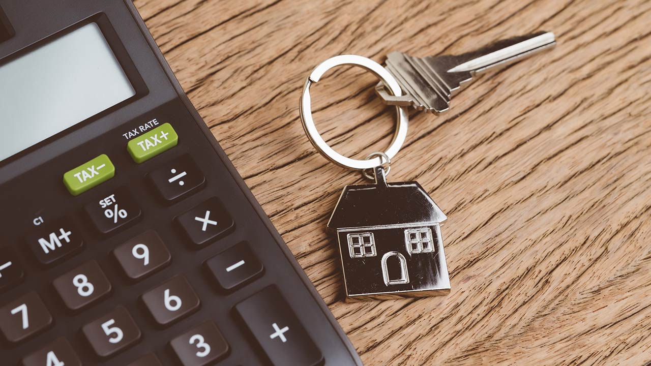 Home key with house keyring with black calculator on wooden table