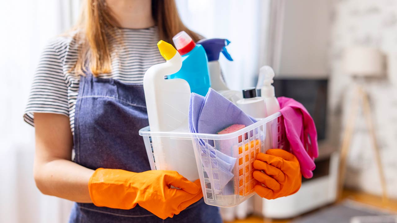 woman in rubber gloves with basket of cleaning supplies ready to clean up her apartment