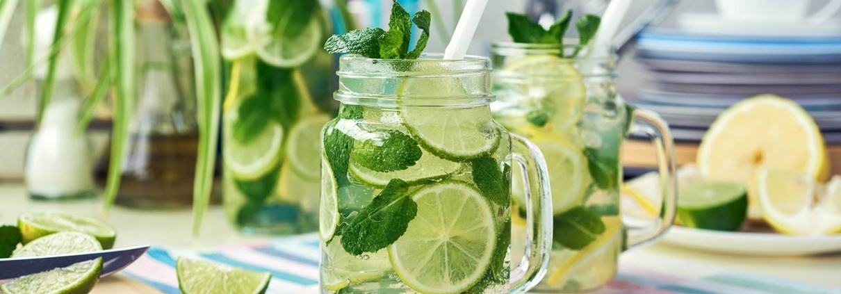 Two glasses and a bottle of homemade lemon, lime, and mint lemonade sit on the wooden dining table