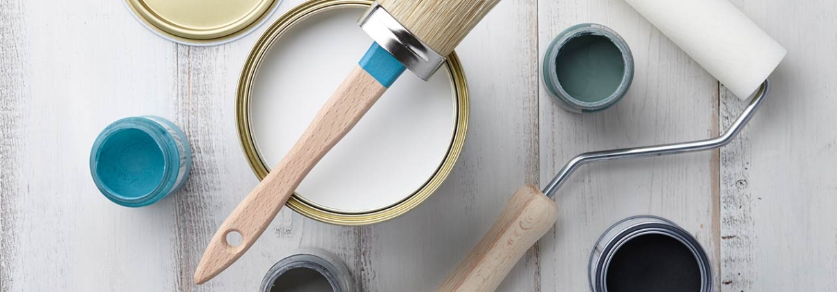 Paint brush, sponge roller, paints, waxes and other painting or decorating supplies on white wooden planks