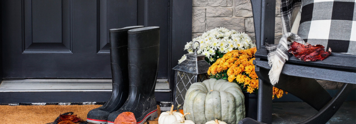 Traditional style front porch decorated for autumn with rain boots, heirloom gourds, white pumpkins, mums and rocking chair