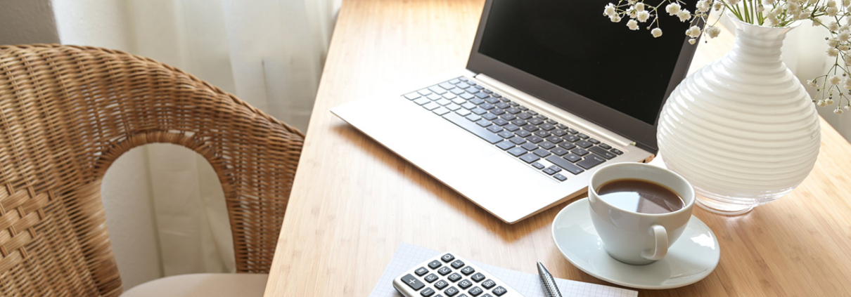 Home office desk with laptop computer, calculator, spiral book, coffee and a white flower bouquet, business accounting concept, copy space, selected focus