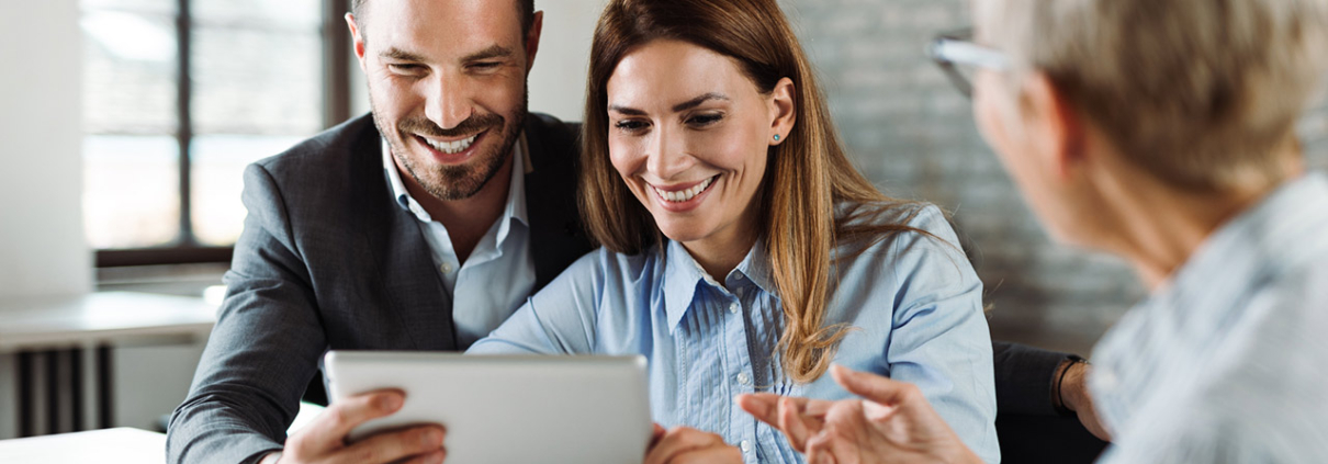 Happy couple using tablet while having a meeting with their real estate agent in the office