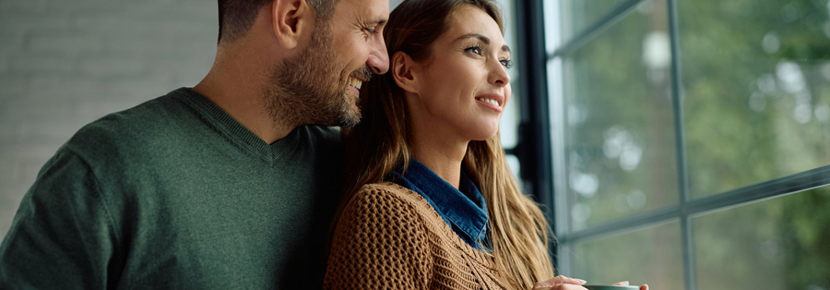 Smiling woman day dreaming while drinking coffee with her husband by the window at home